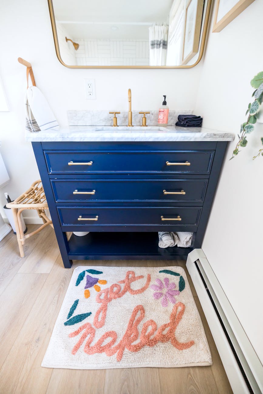 Elegant bathroom with chic vanity and a playful 'get naked' rug, perfect for modern interiors.