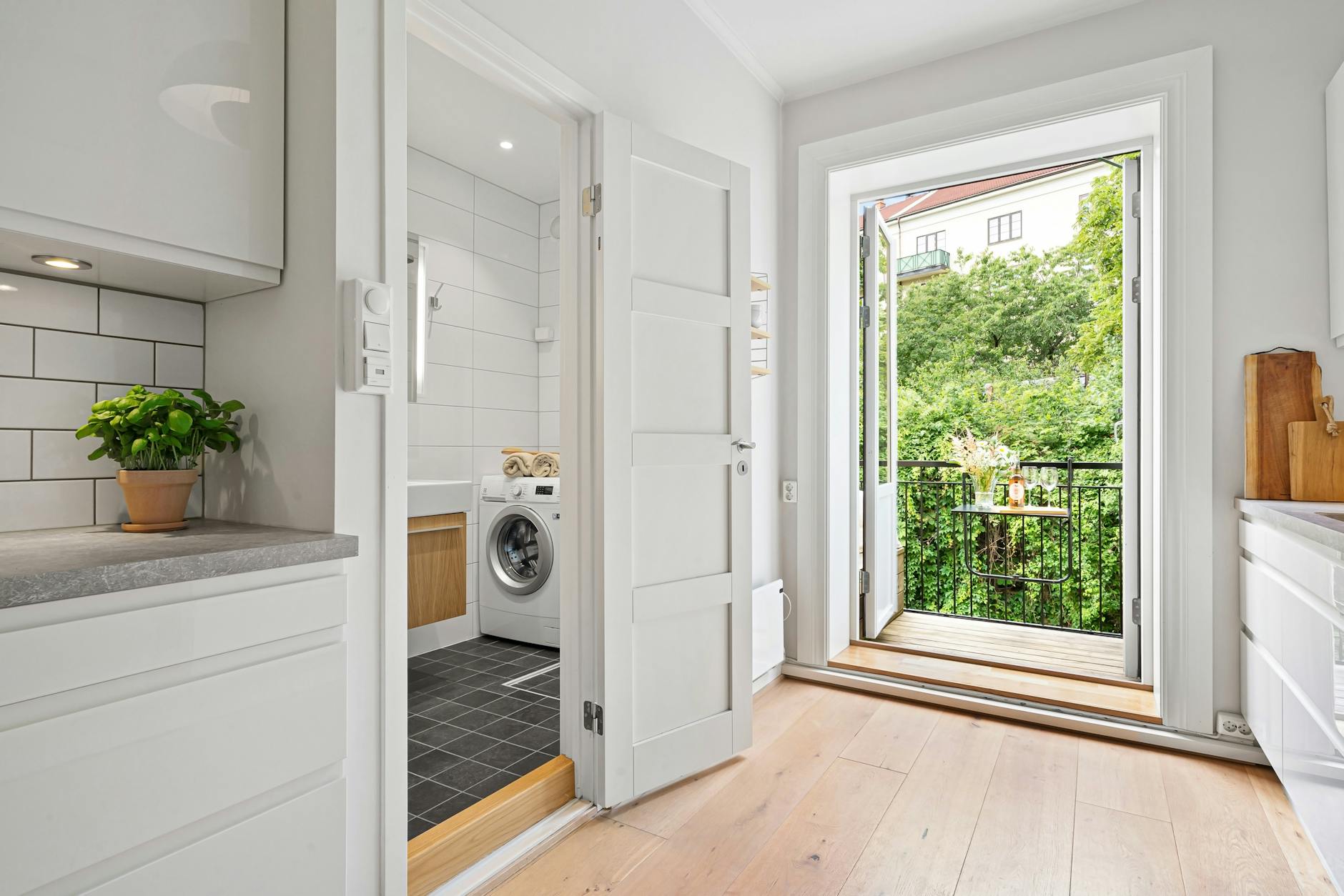 Contemporary apartment kitchen and laundry area with balcony overlooking lush greenery.