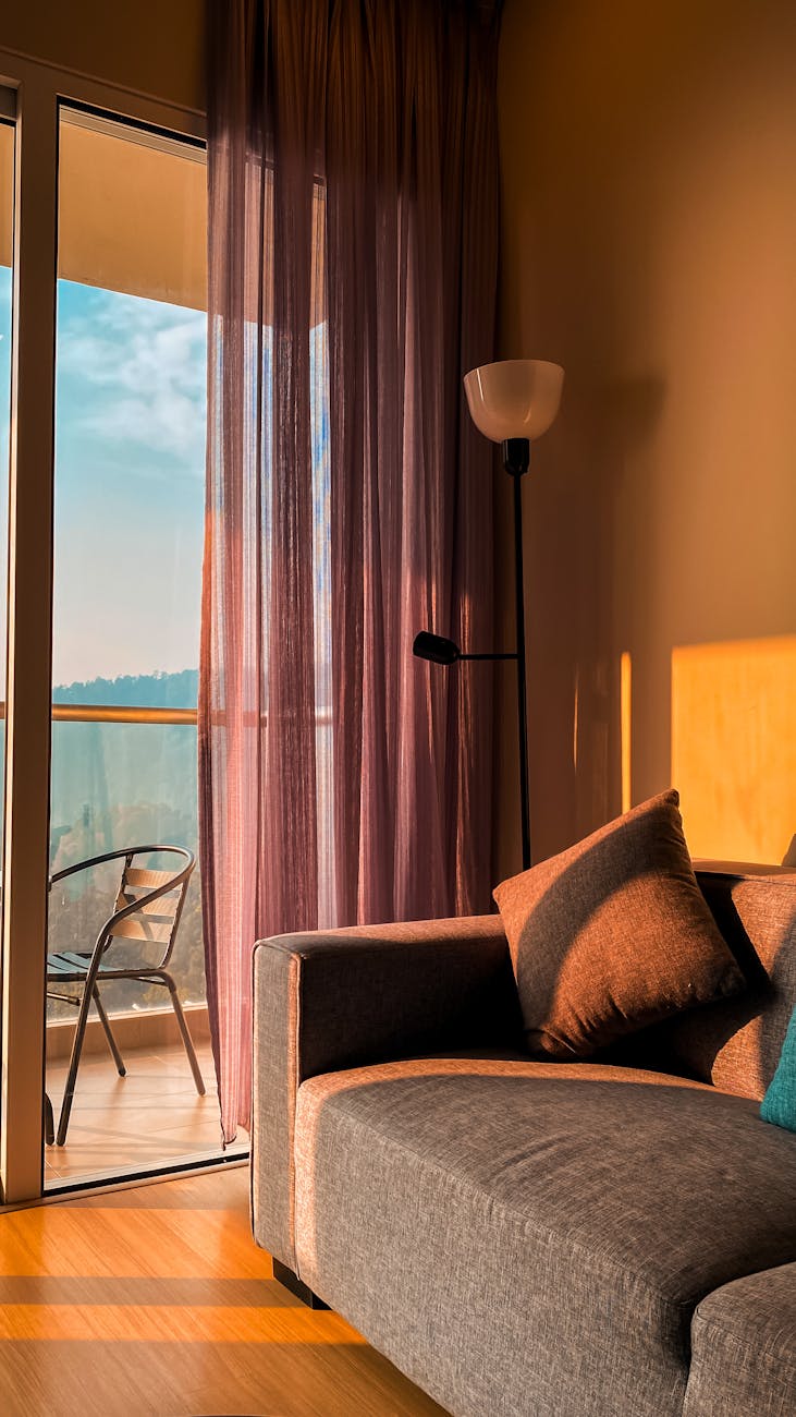 Warm sunlight fills a modern indoor space with a cozy sofa and balcony view.
