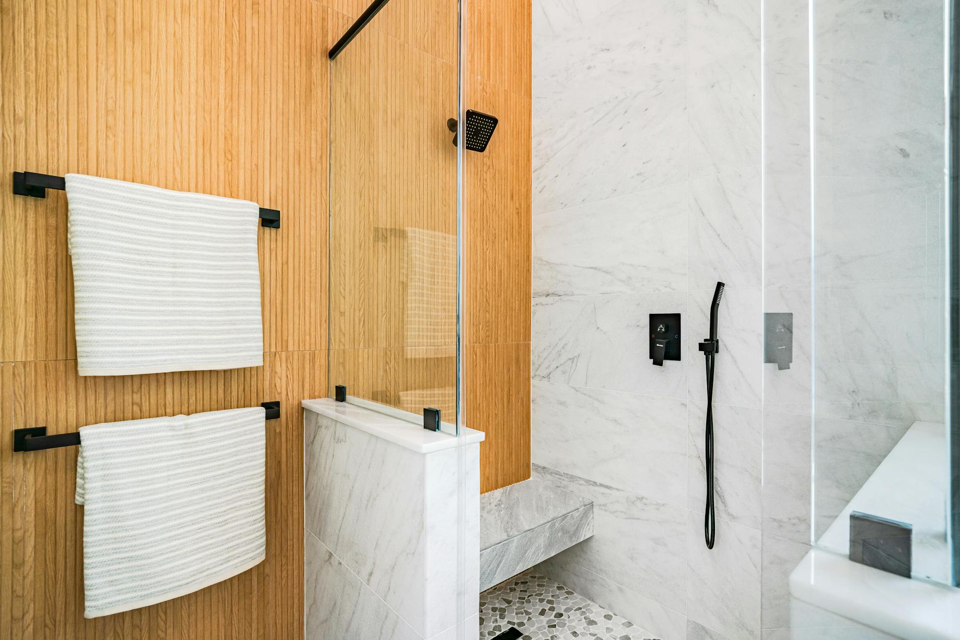 Elegant modern bathroom featuring marble tiles, wood paneling, and glass shower door.
