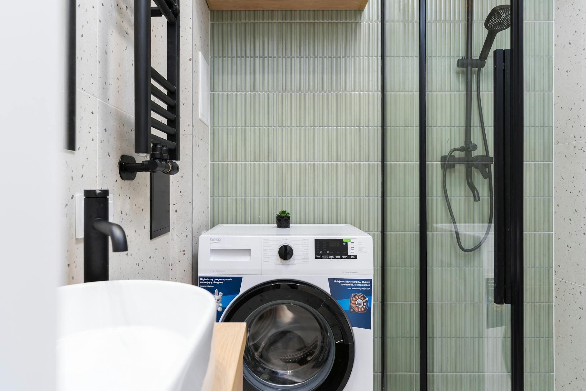 Sleek bathroom design featuring a washing machine, shower, and basin in Kraków.
