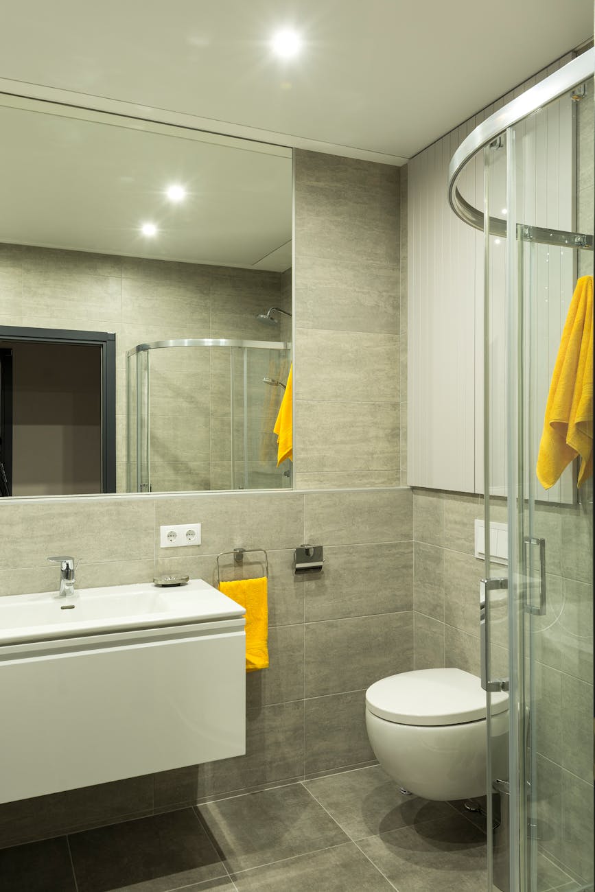 Sleek modern bathroom with a shower, sink, and toilet, featuring yellow towels for a pop of color.
