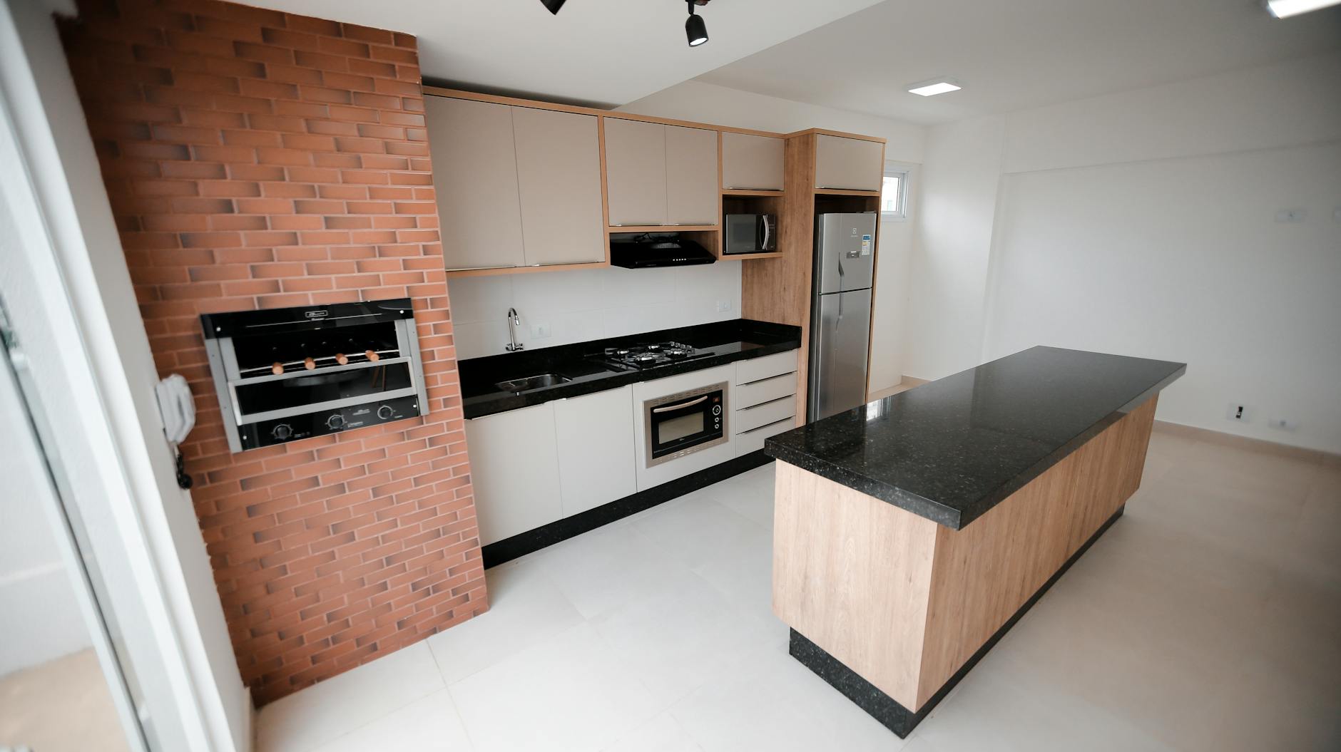 Contemporary kitchen interior featuring a brick wall, sleek countertops, and a central island.
