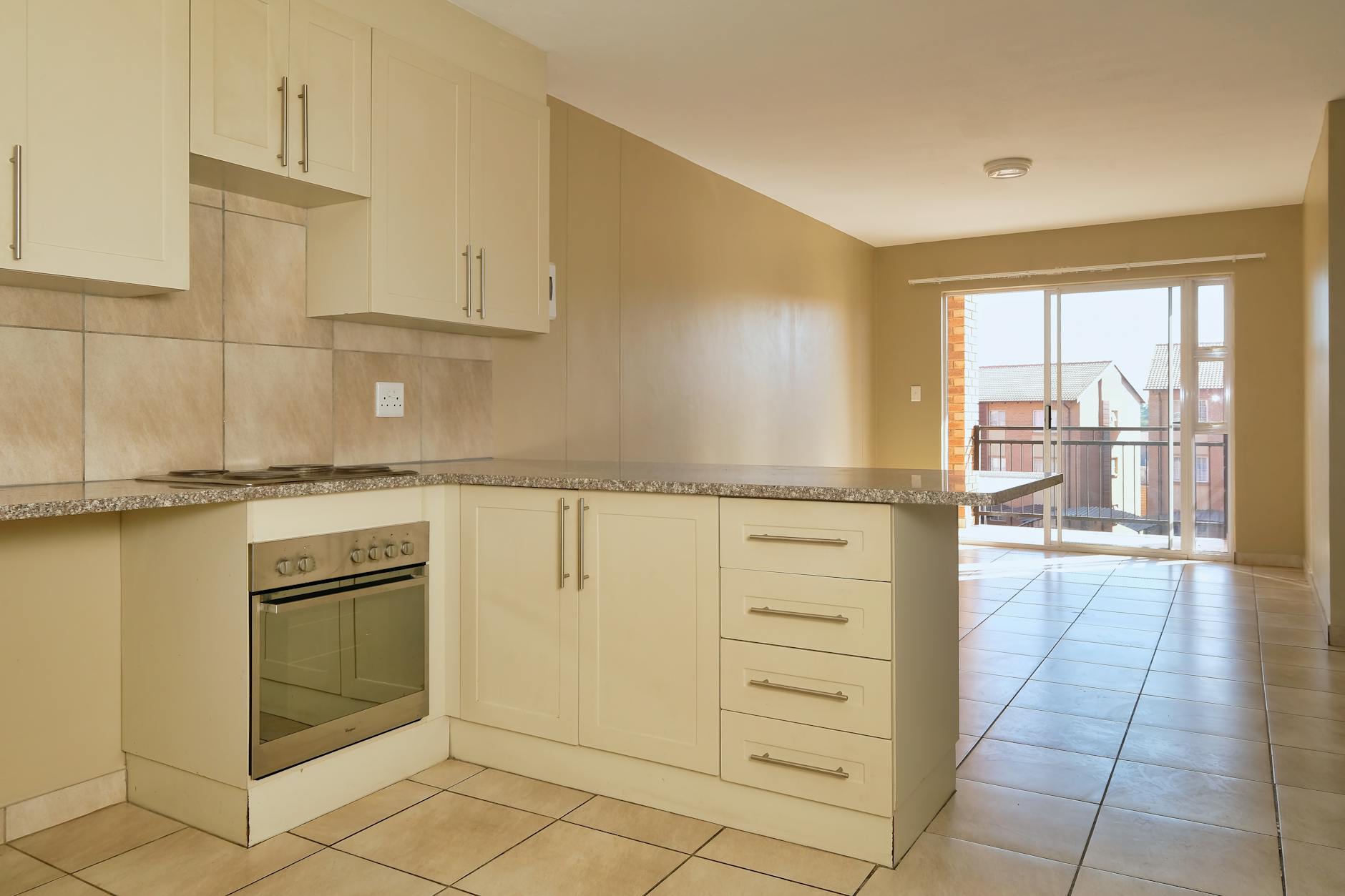 Bright modern kitchen with granite countertops and sunlit balcony view, showcasing elegant cabinetry.