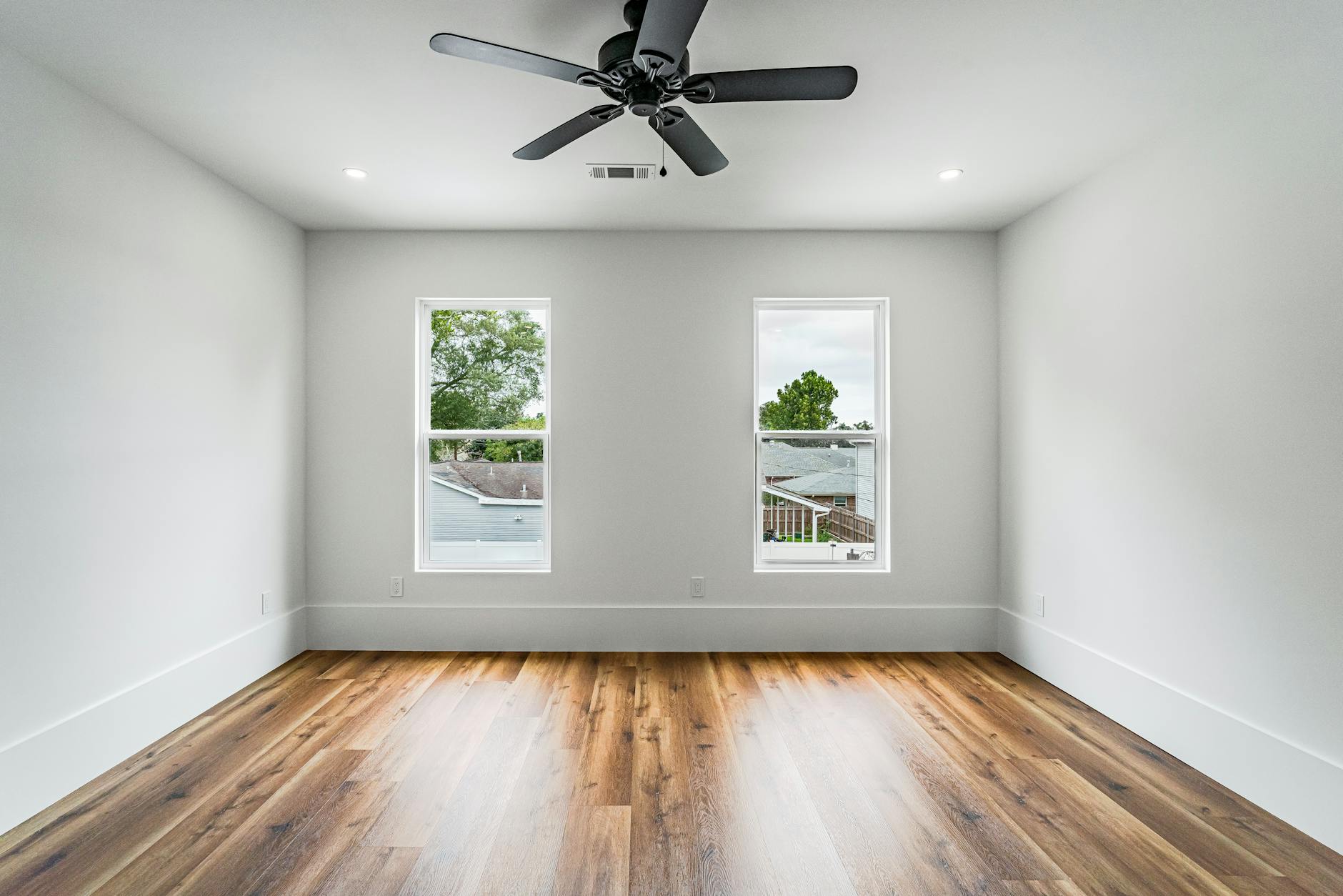 Modern minimalist bedroom featuring a ceiling fan and natural light from two windows in New Orleans.